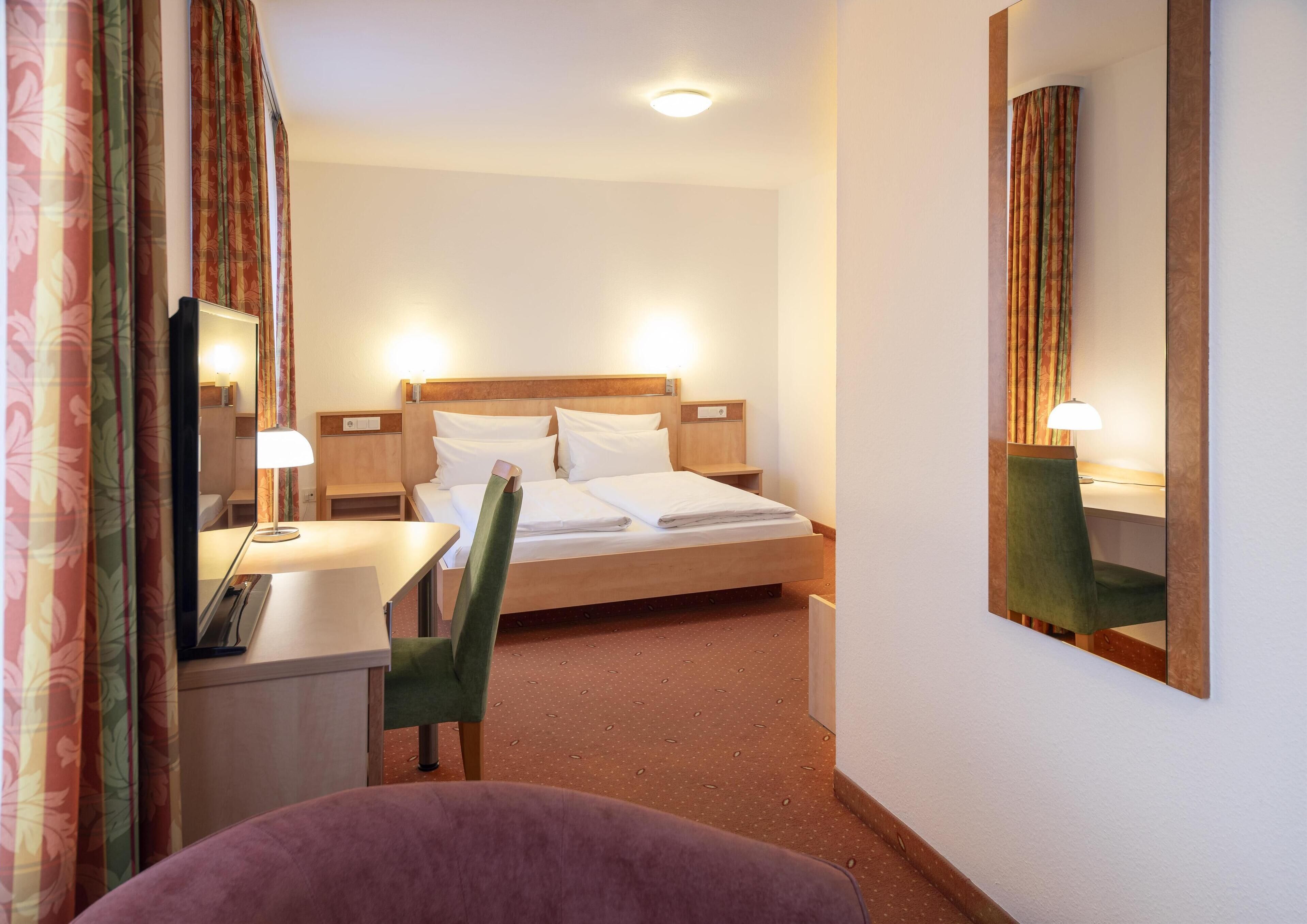 A hotel room with a bed, a desk, a chair, and a mirror.