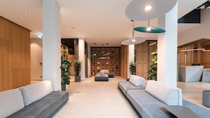 A modern lobby with grey sofas, a bookshelf, and pendant lighting.