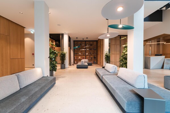 A modern lobby with grey sofas, a bookshelf, and pendant lighting. -  ZELLER's Quartier (Koenigsbrunn)