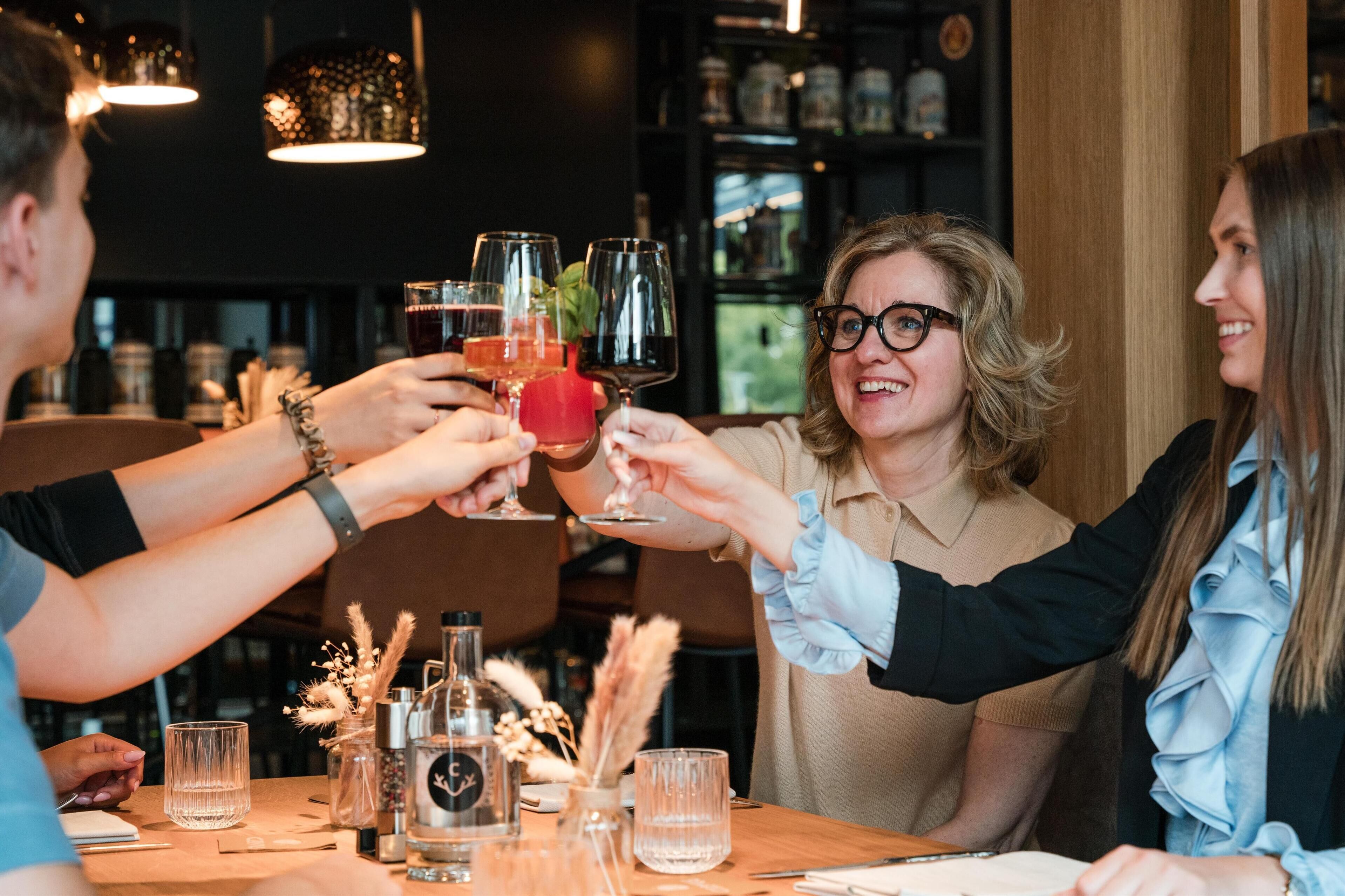 Un grupo de personas brindando con bebidas sentadas en una mesa en un restaurante con decoración de madera e iluminación colgante.