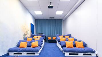 Ein Raum mit blauen Massagesesseln, orangefarbenen Kissen, einem Projektor an der Decke und einem blauen Vorhang im Hintergrund.