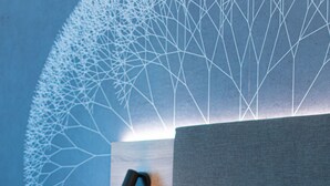 A neatly made bed with white linens, a headboard with a geometric light design, and a wall-mounted lamp. - Taste Hotel Jettingen (Jettingen-Scheppach)