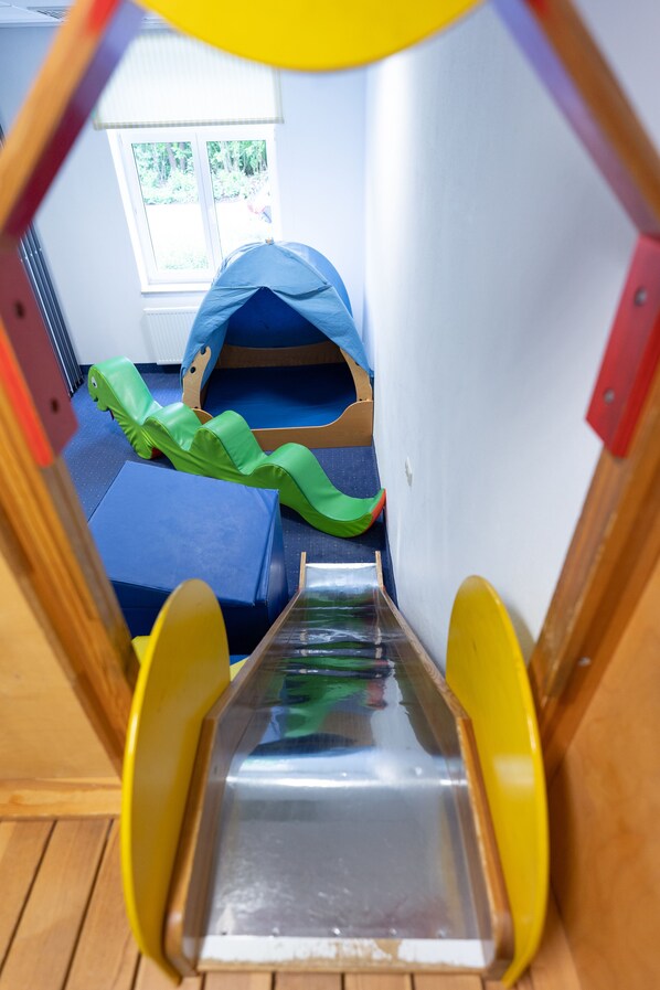 A children's play area with a slide, bunk beds, and a window with a view of greenery.