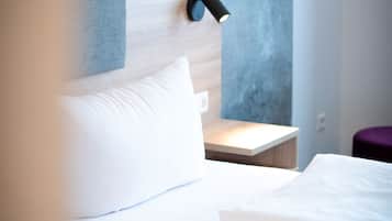 Ein modernes Hotelzimmer mit einem ordentlich bezogenen Bett, einem kleinen Nachttisch und einer Wandleuchte.