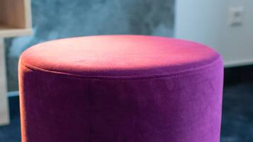 Um banquinho roxo num quarto com carpete azul e parede cinza com textura.