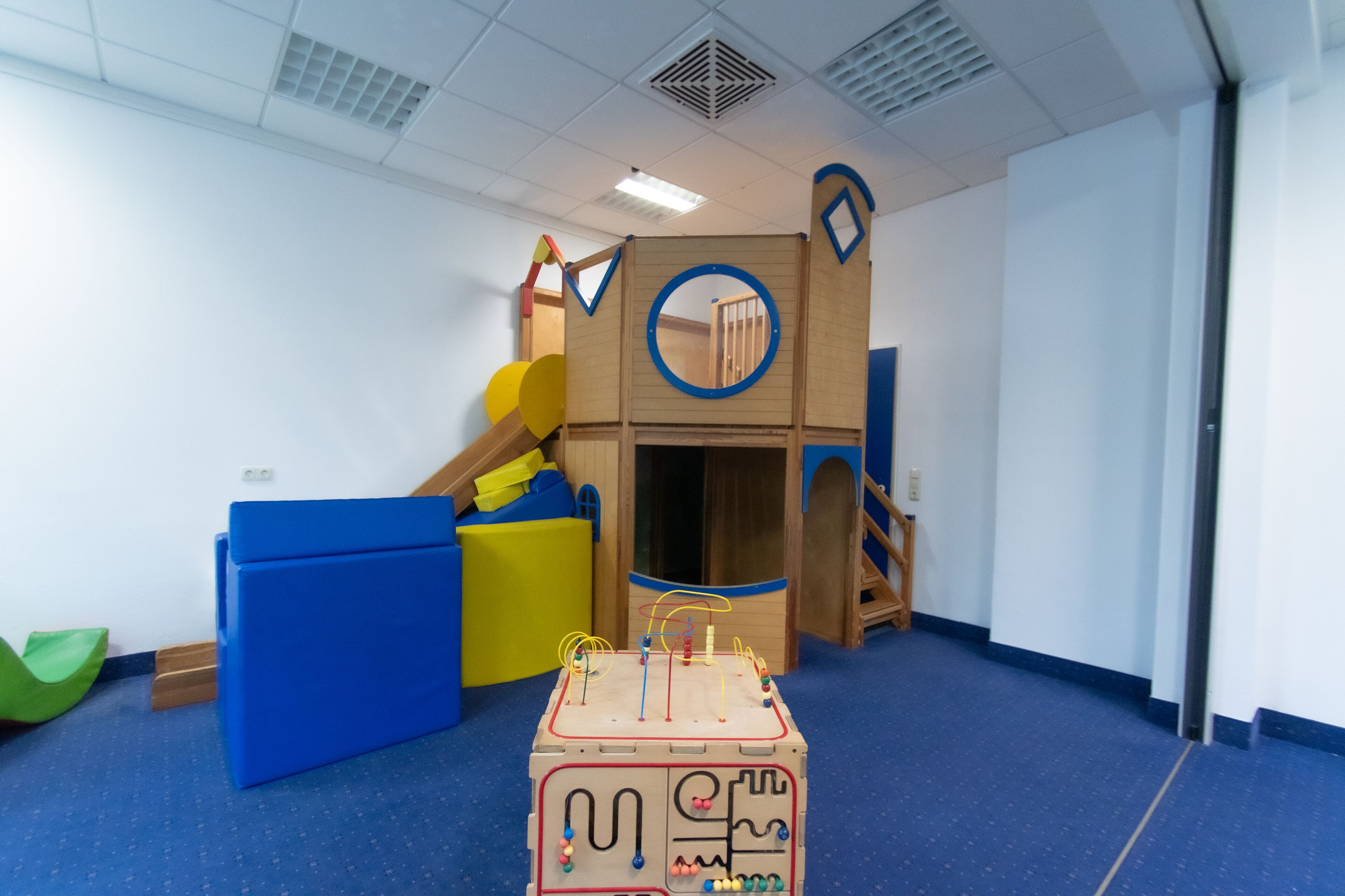 Zona de juegos con tobogán, pared de escalar y casita de madera.