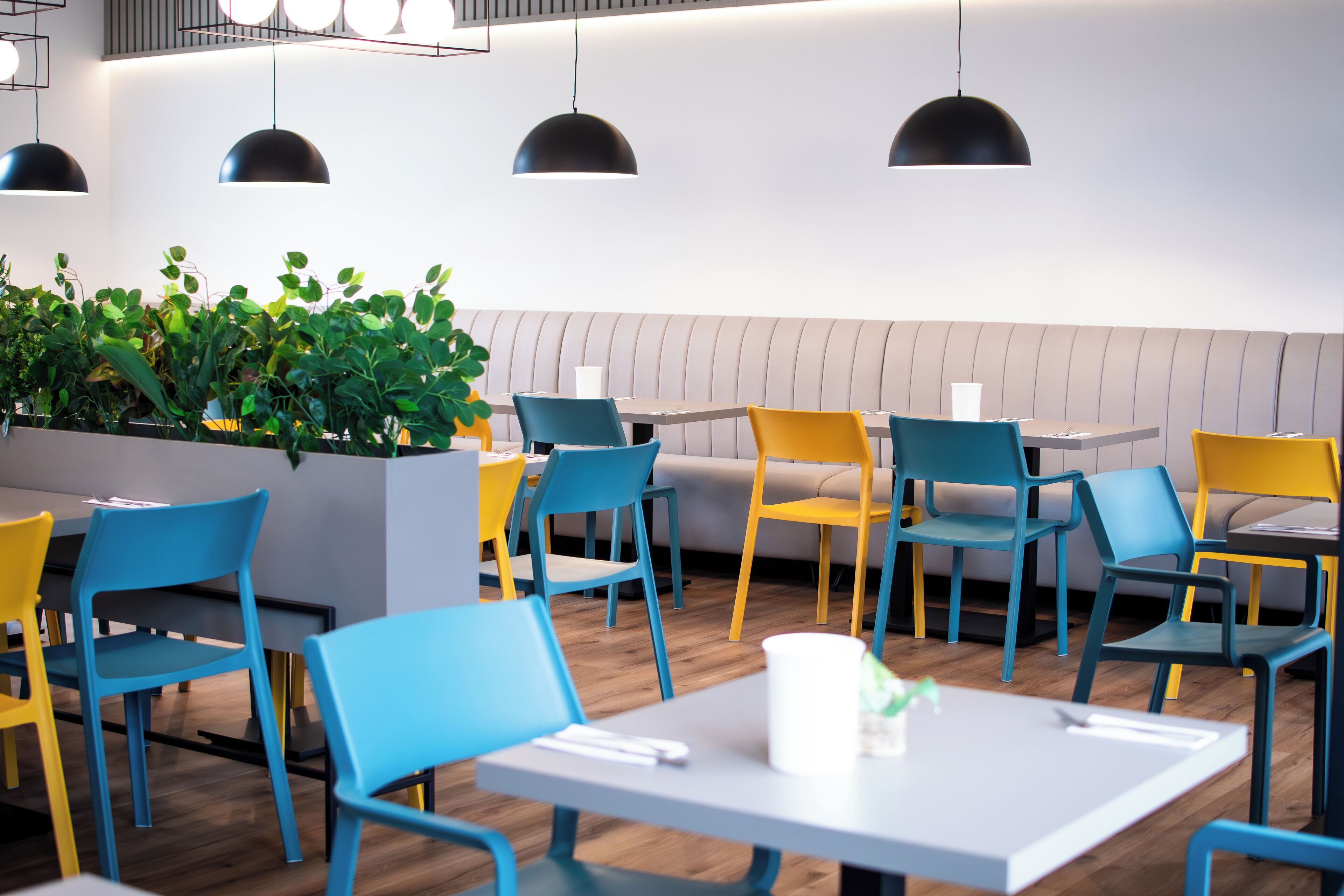 A modern restaurant interior with multiple tables and chairs, a seating area with a cushioned bench, and pendant lighting.