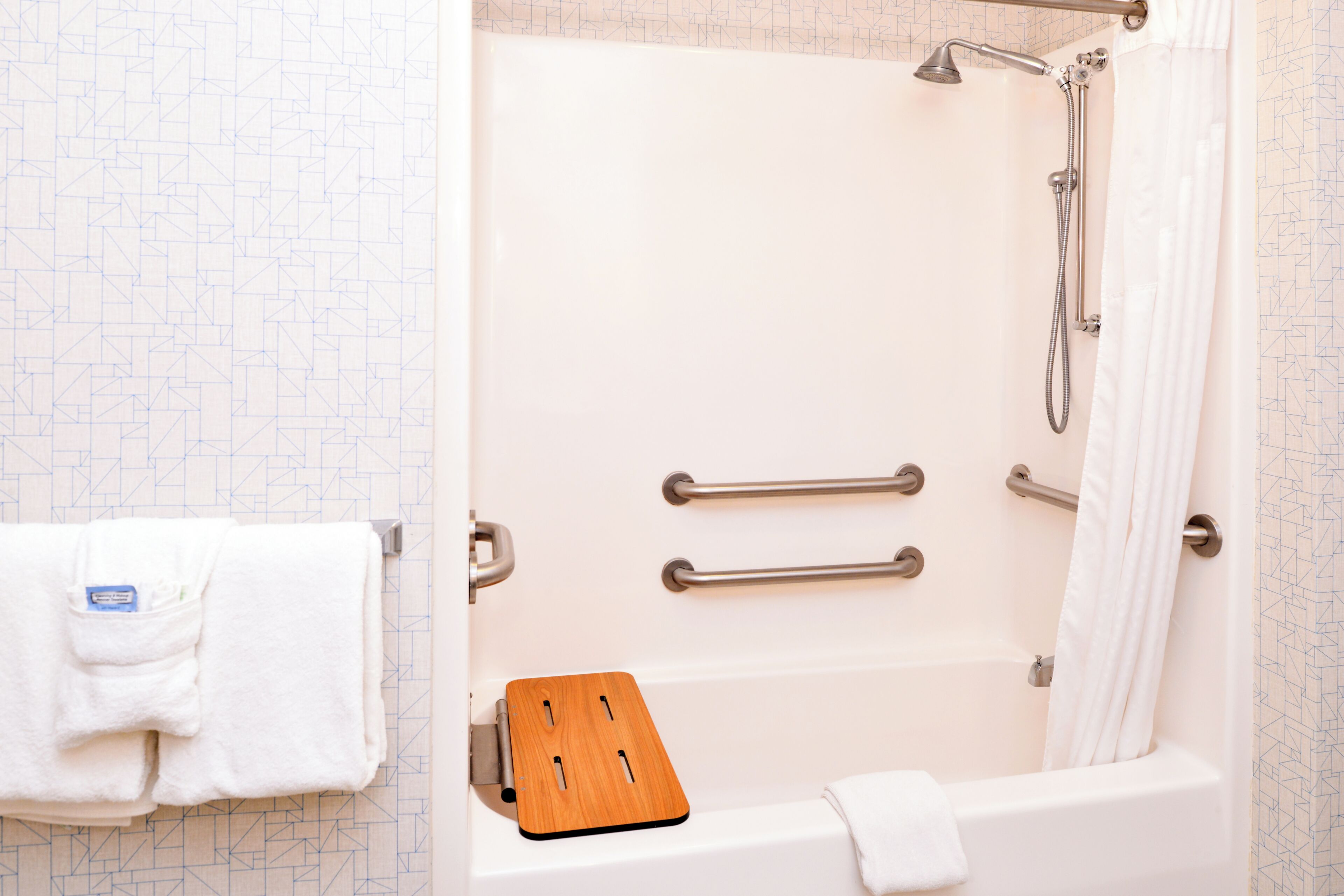 A bathroom with a bathtub, a shower, and a wooden bath mat.