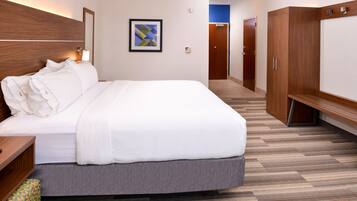 Una habitación de hotel con una cama, cabecera de madera, una obra de arte abstracta en marco, un armario y una puerta que da a otra habitación.