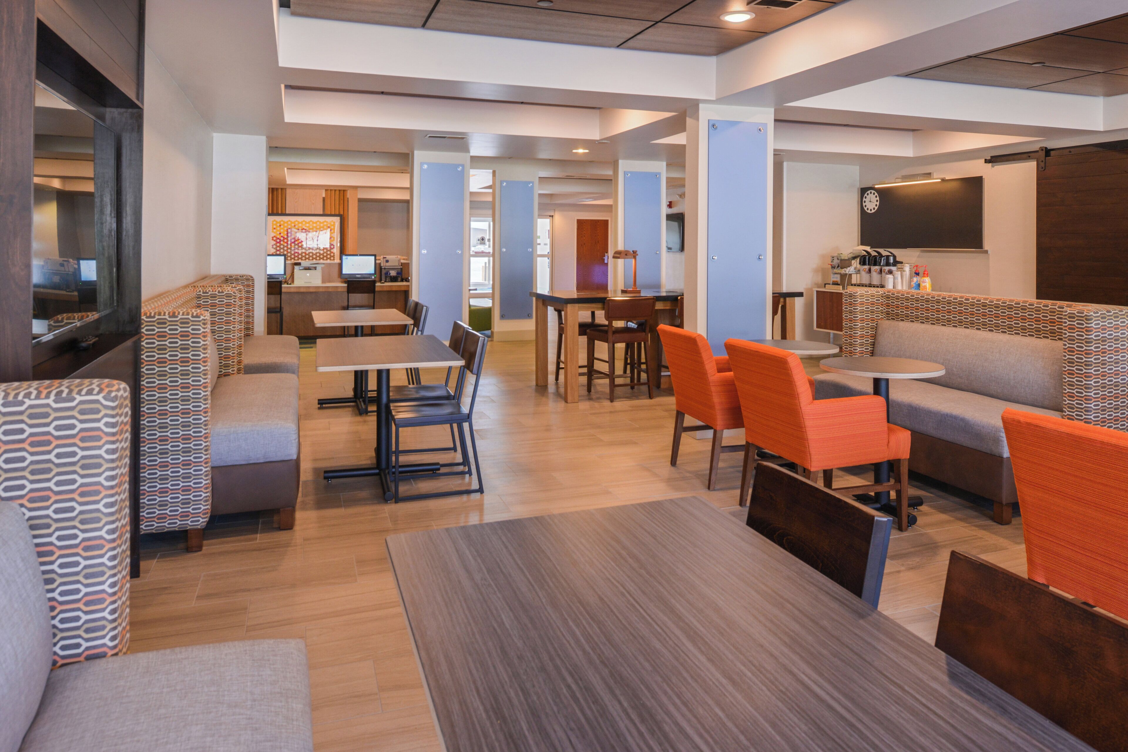 A modern hotel lobby with seating areas, a reception desk, and a television screen.