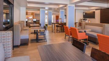 A modern hotel lobby with seating areas, a reception desk, and a television screen.