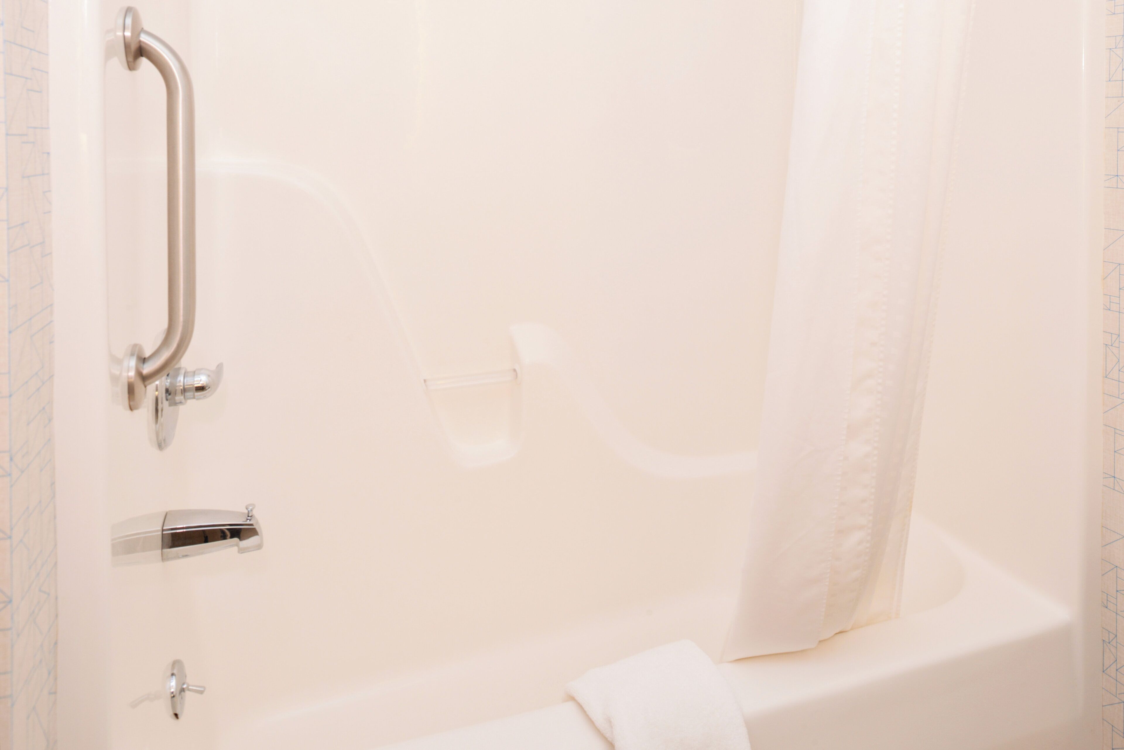 Een badkamer met een douche, een handgreep, een glazen vaas en een handdoek.