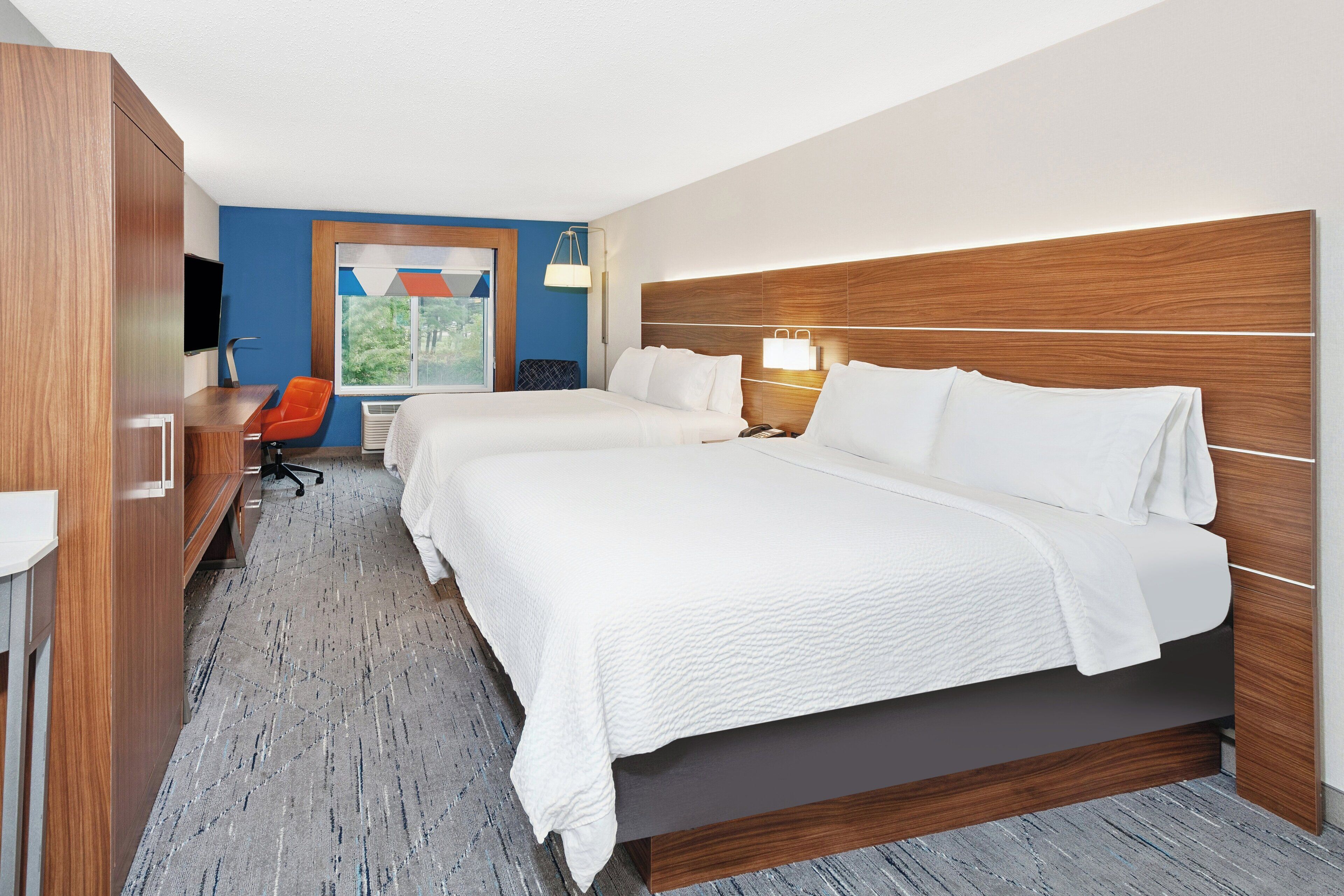 Une chambre d’hôtel avec un grand lit, un bureau avec une chaise, une télévision et une fenêtre donnant sur un paysage verdoyant.
