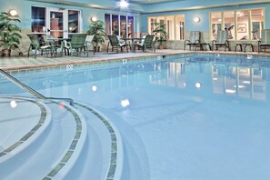 Una piscina interior con borde de azulejos, rodeada de sillas y plantas en macetas.