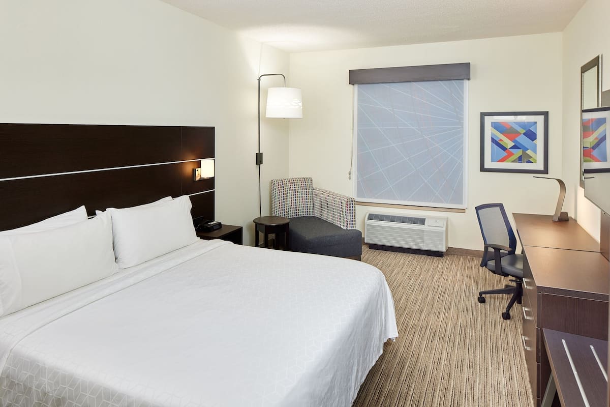 A hotel room with a large bed, a desk, a chair, a lamp, and a window with a view.