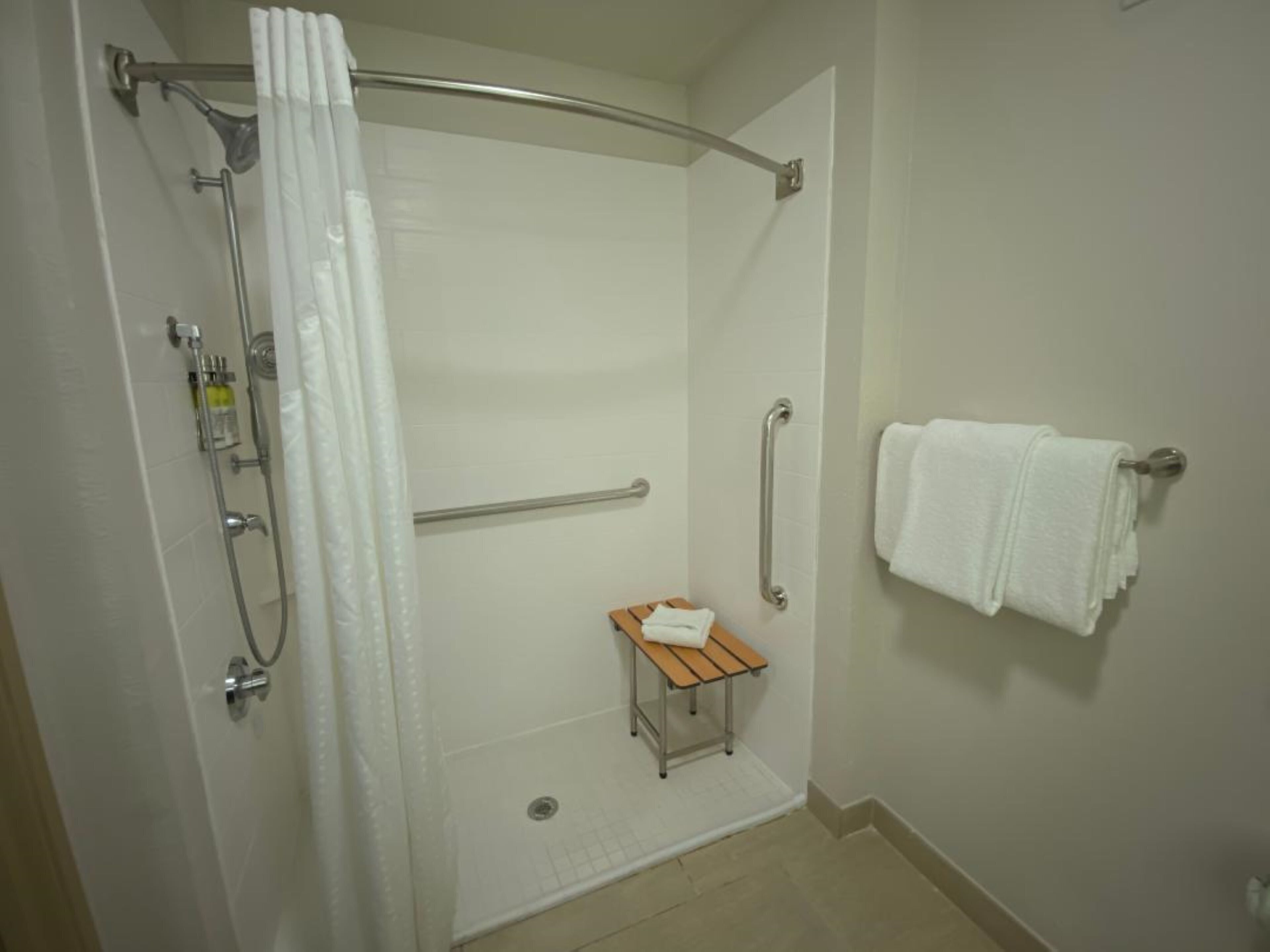 Un espacio de ducha con barra de apoyo, un banco de madera pequeño y un perchero para toallas.
