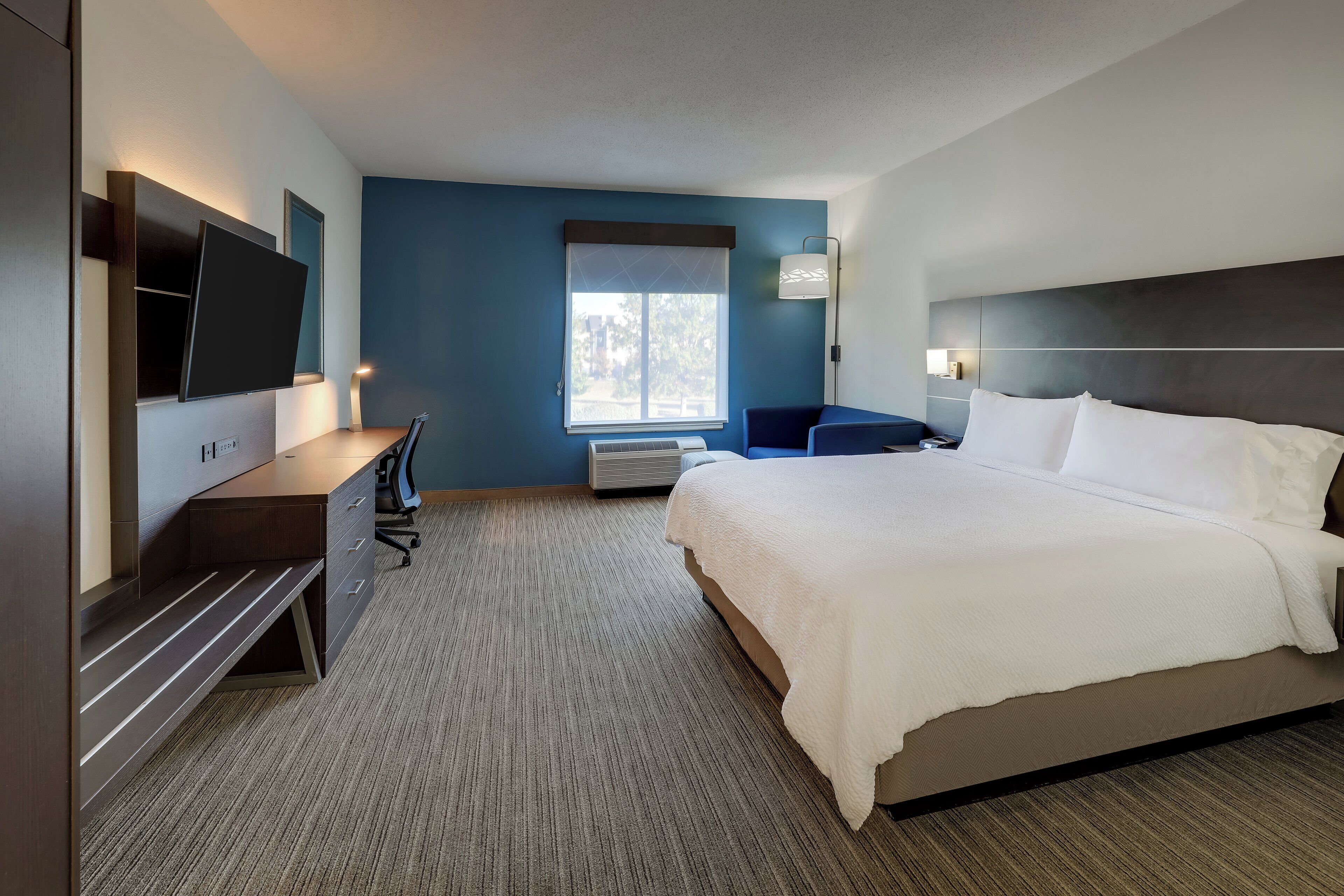 A hotel room with a bed, desk, chair, TV, and window.