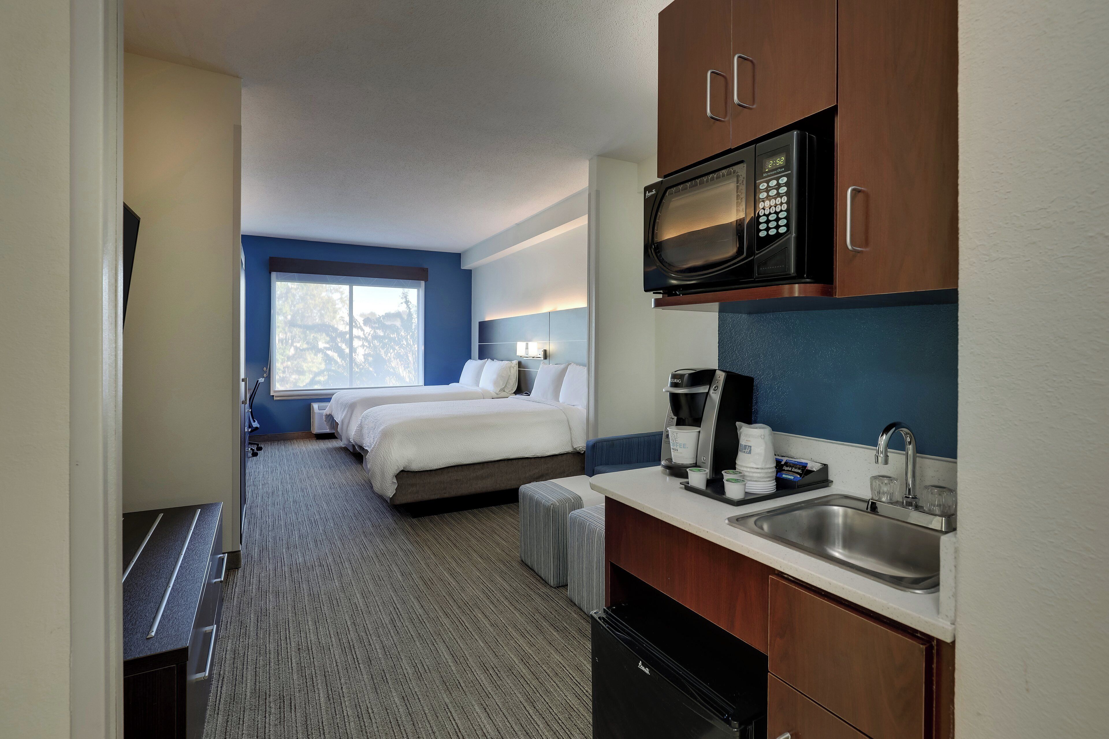 Une chambre d’hôtel équipée d’une kitchenette, d’un lit, d’une fenêtre et offrant une vue sur les arbres.