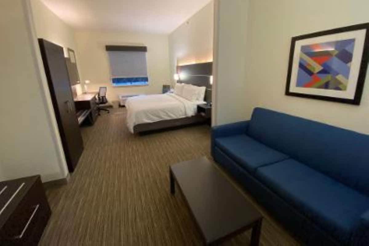 A hotel room with a bed, a blue sofa, a small table, and a framed picture on the wall.