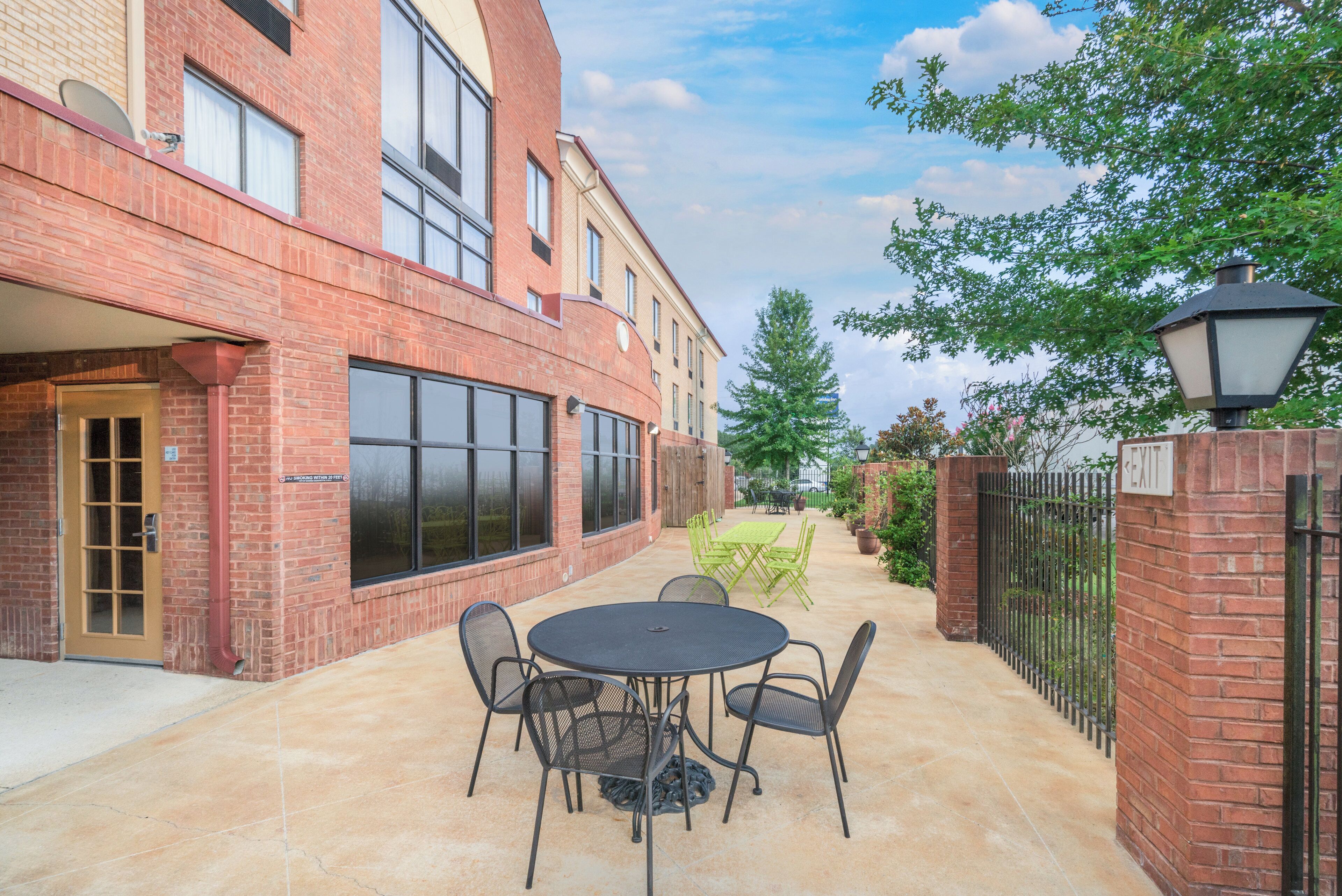 A patio area with a round table and chairs, a brick building, and a metal fence.
