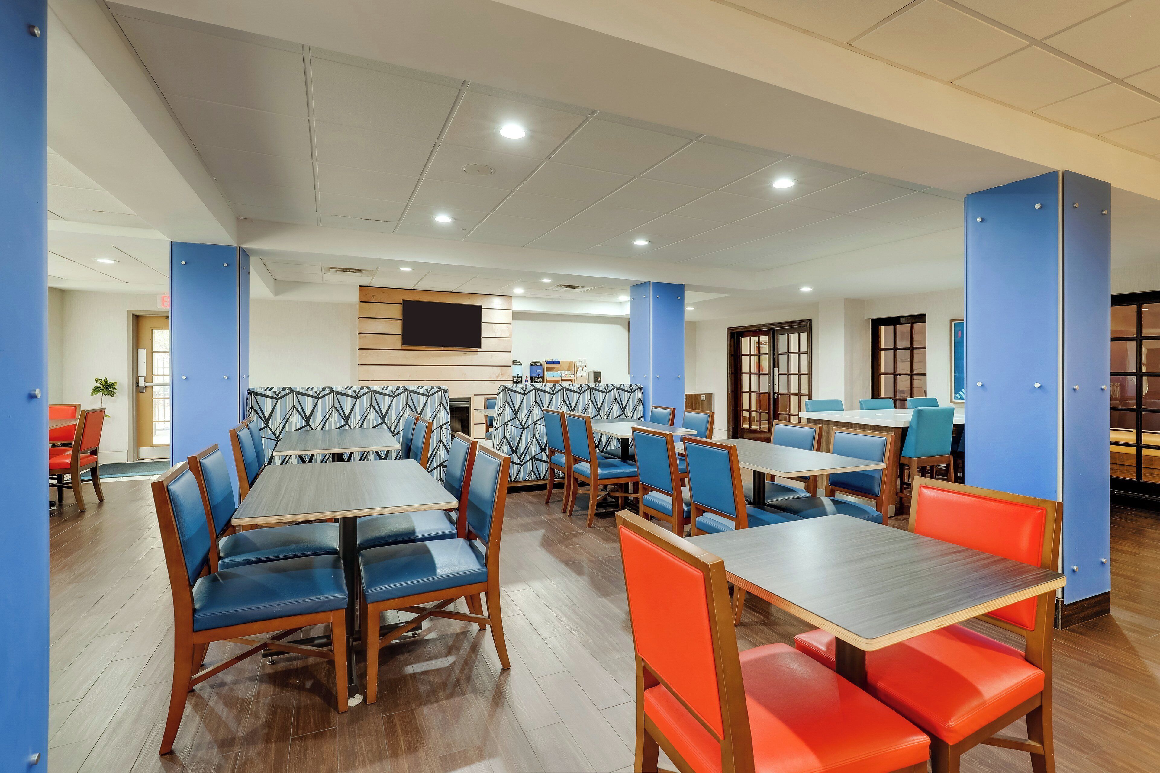 A modern dining area with wooden tables and chairs, a counter, and a TV mounted on the wall.