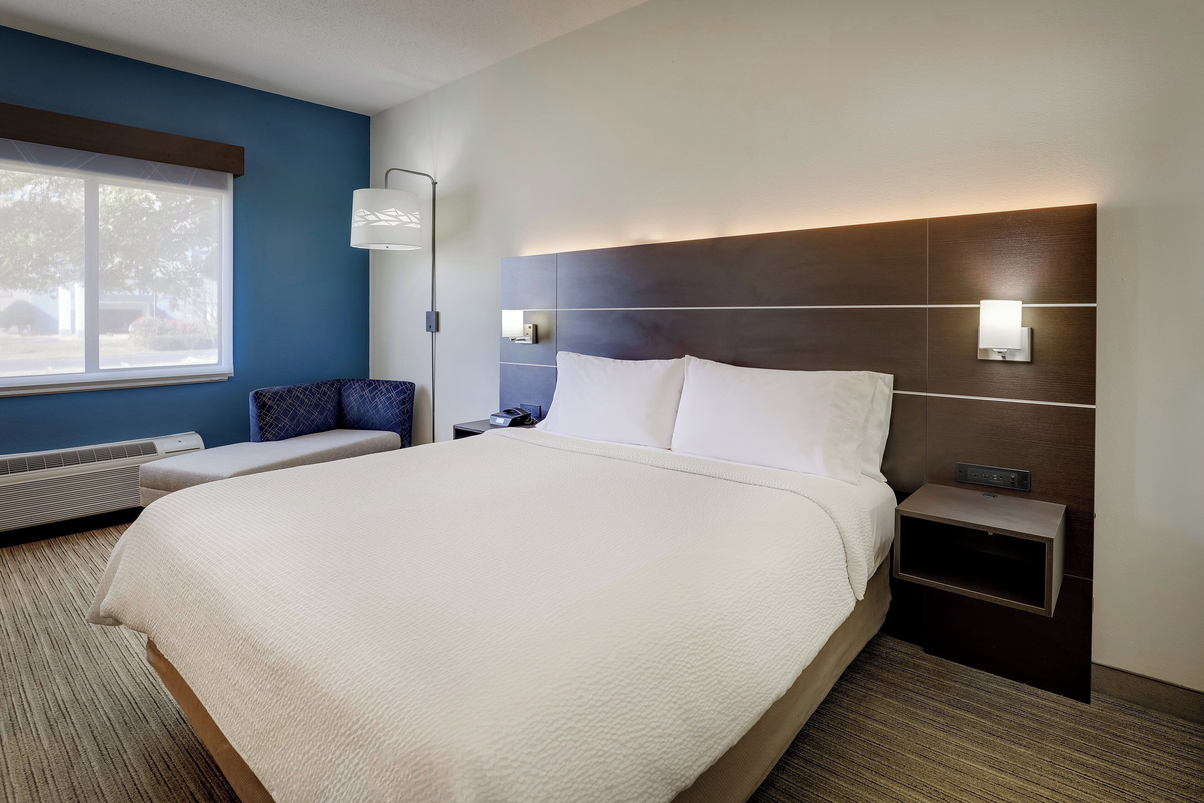 A hotel room with a large bed, a bedside table, a lamp, and a window.