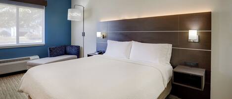 Una habitación de hotel con una cama grande, una mesita de noche, una lámpara y una ventana.
