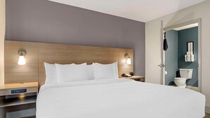 A modern hotel room with a large bed, wooden headboard, bedside tables, and a nightstand with a lamp.