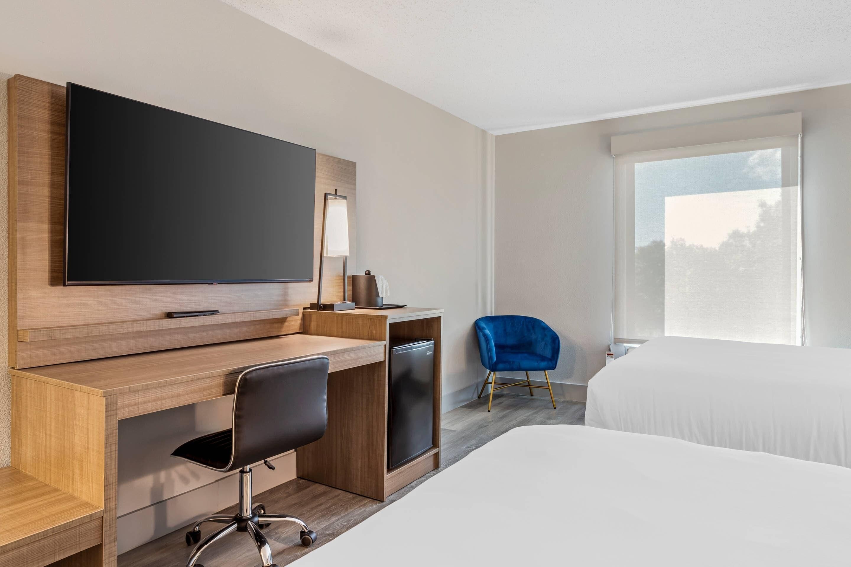 Une chambre d’hôtel comprenant un lit, un bureau avec une chaise, une télévision et une fenêtre.