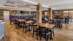 A spacious restaurant with wooden flooring, multiple tables and chairs, a bar area, and a neon sign.