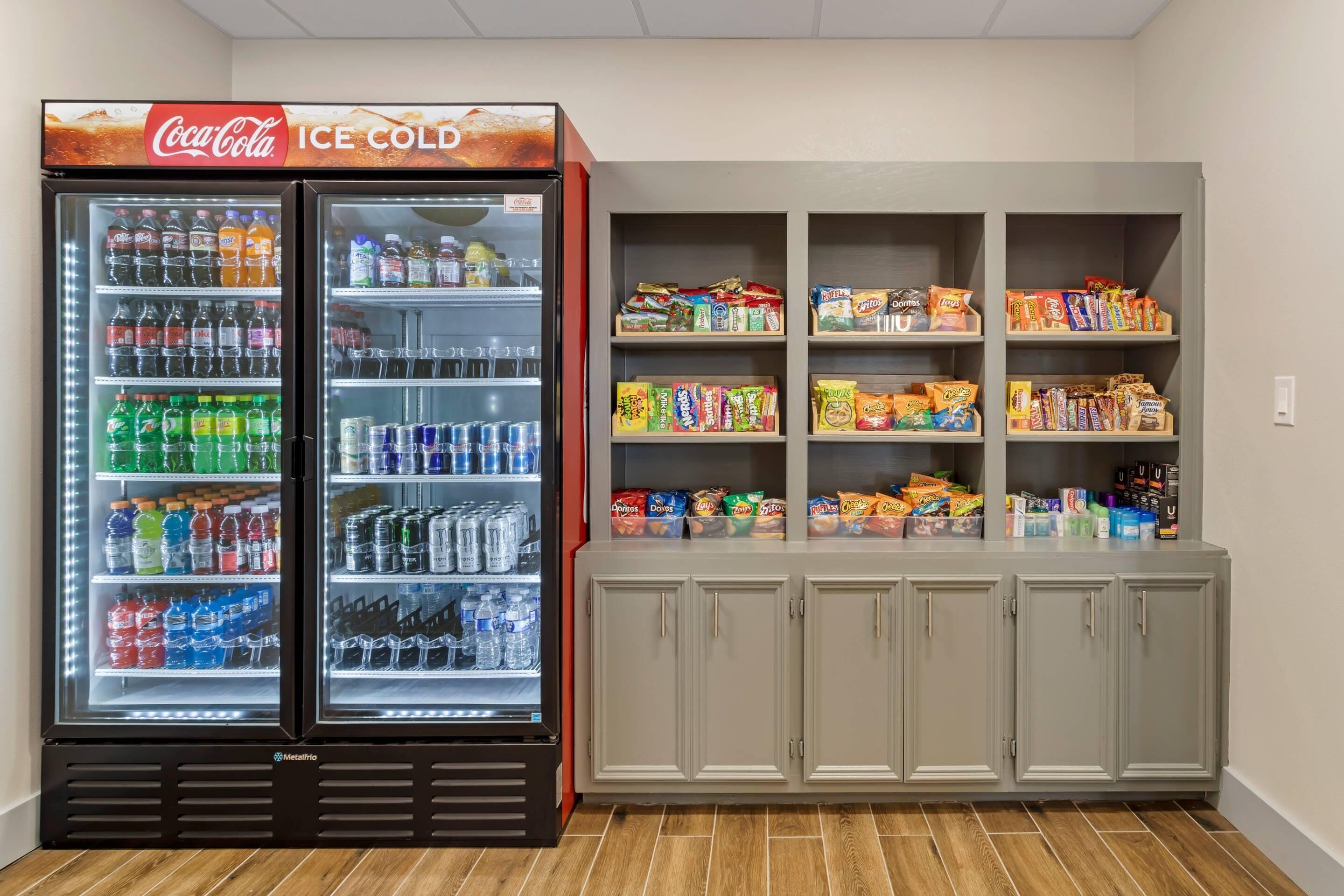 A vending machine with a Coca-Cola sign, a refrigerator stocked with beverages, and a snack cabinet with various packaged foods.
