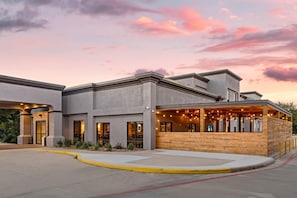 A modern building with a covered outdoor seating area, large windows, and a well-maintained entrance.