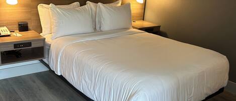 Un dormitorio moderno con una cama grande, cabecera de madera, dos mesitas de noche con lámparas, una mesita auxiliar y un estante empotrado.