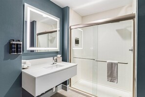 A modern bathroom with a large mirror, white sink, and a glass-enclosed shower.