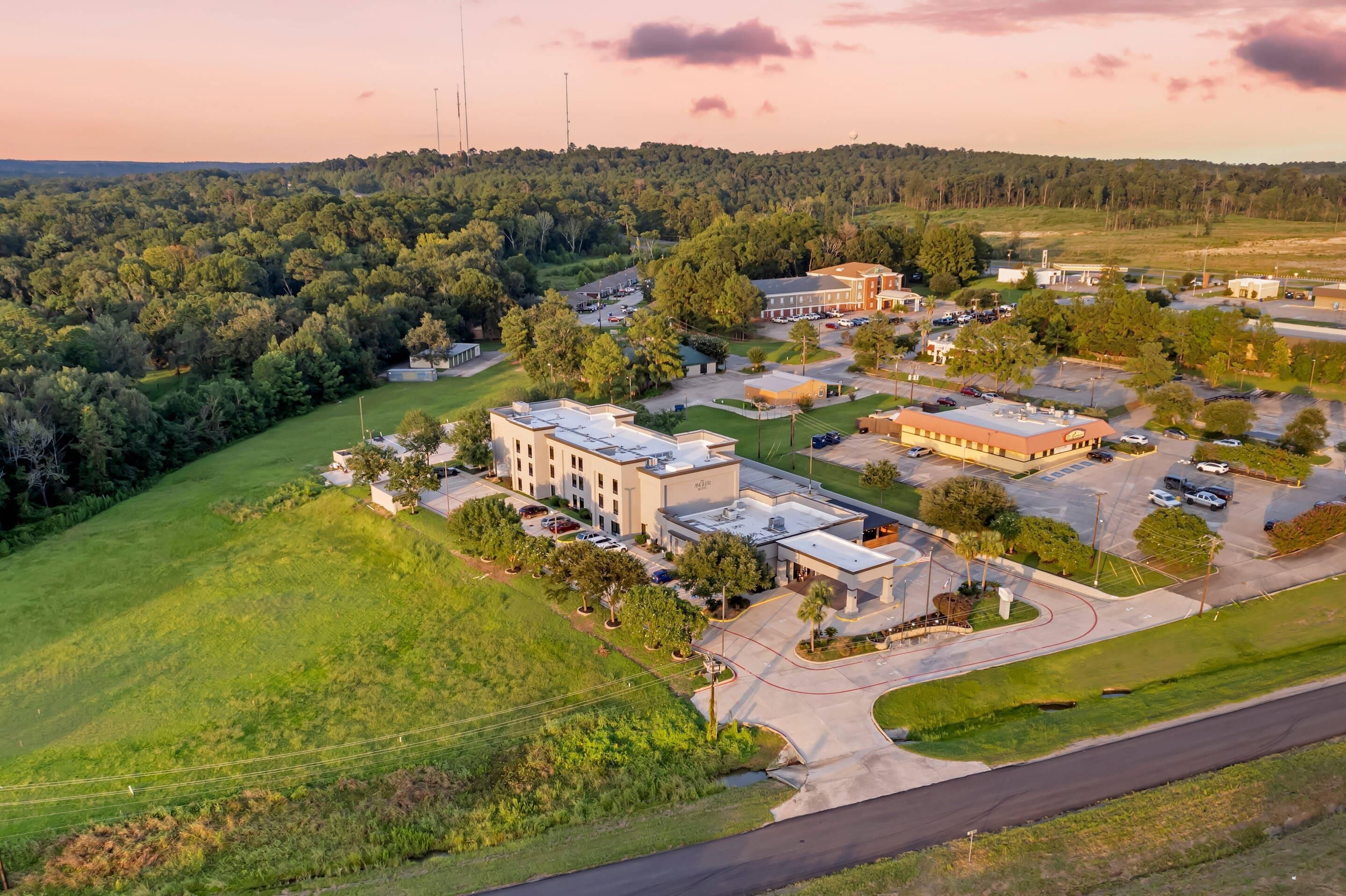 An aerial view of a campus with multiple buildings, parking areas, and surrounding greenery.