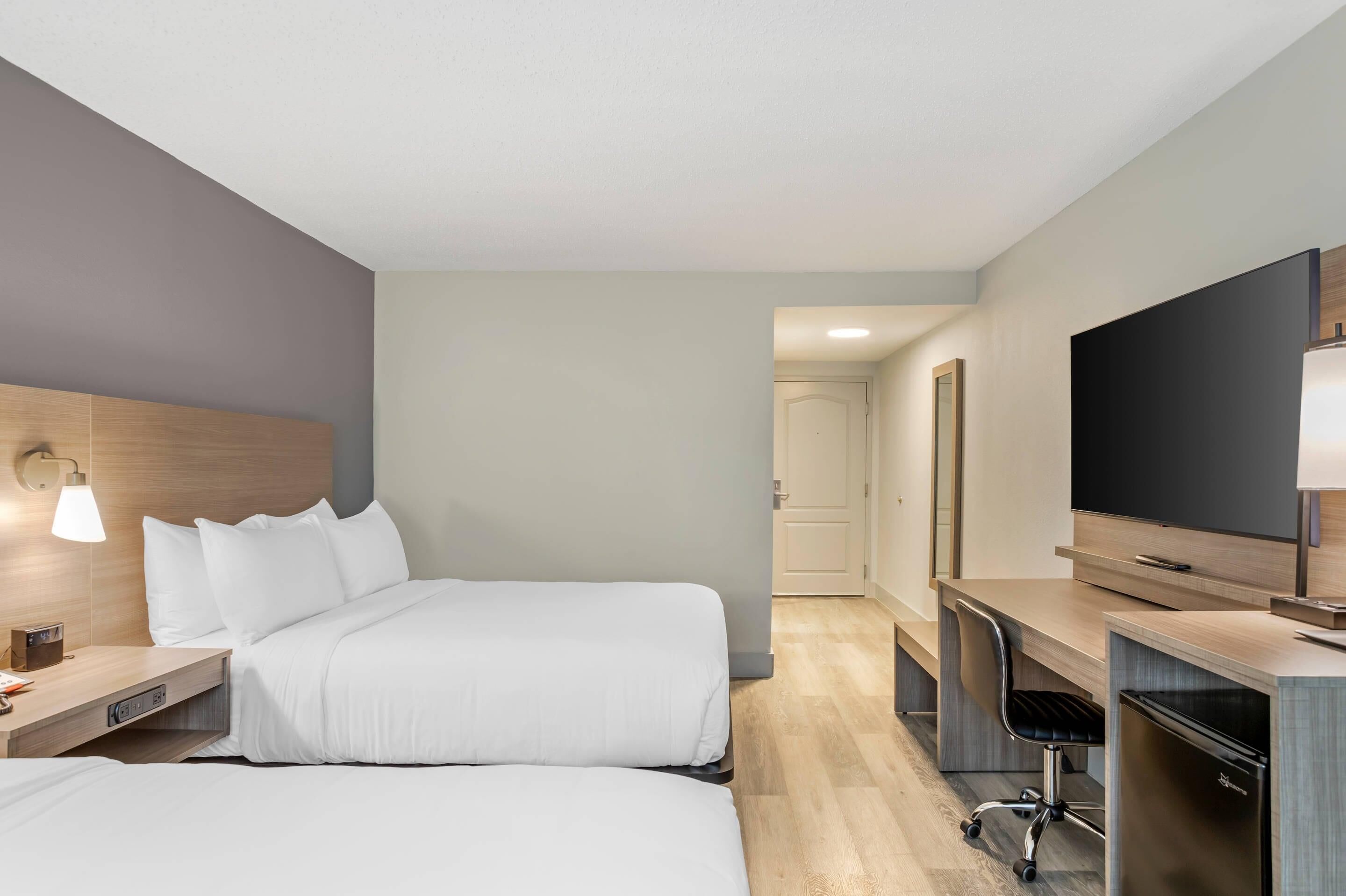 A hotel room with two beds, a desk, a TV, and a lamp.
