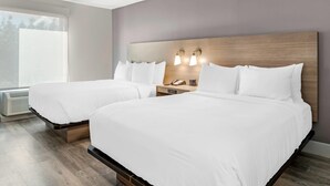 A hotel room with two beds, a wooden headboard, bedside lamps, a telephone, and a window with blinds.