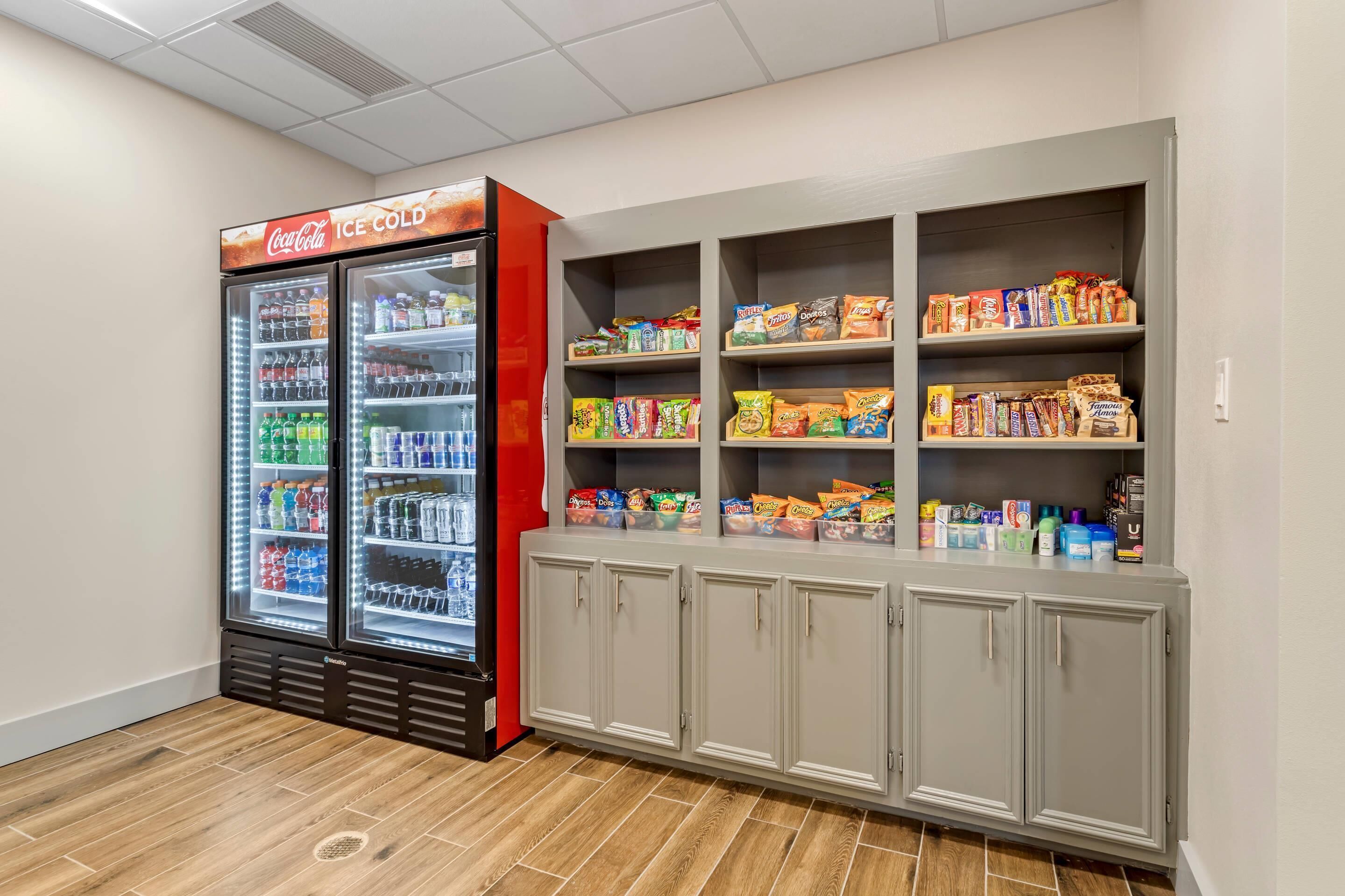 Un distributeur automatique orné d’une enseigne Coca-Cola, rempli de diverses boissons. À côté se trouve un présentoir de collations et de boissons, doté de plusieurs étagères.