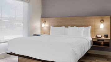 A hotel room with a large bed, wooden headboard, bedside lamps, a nightstand with a phone and clock, and a window with blinds.