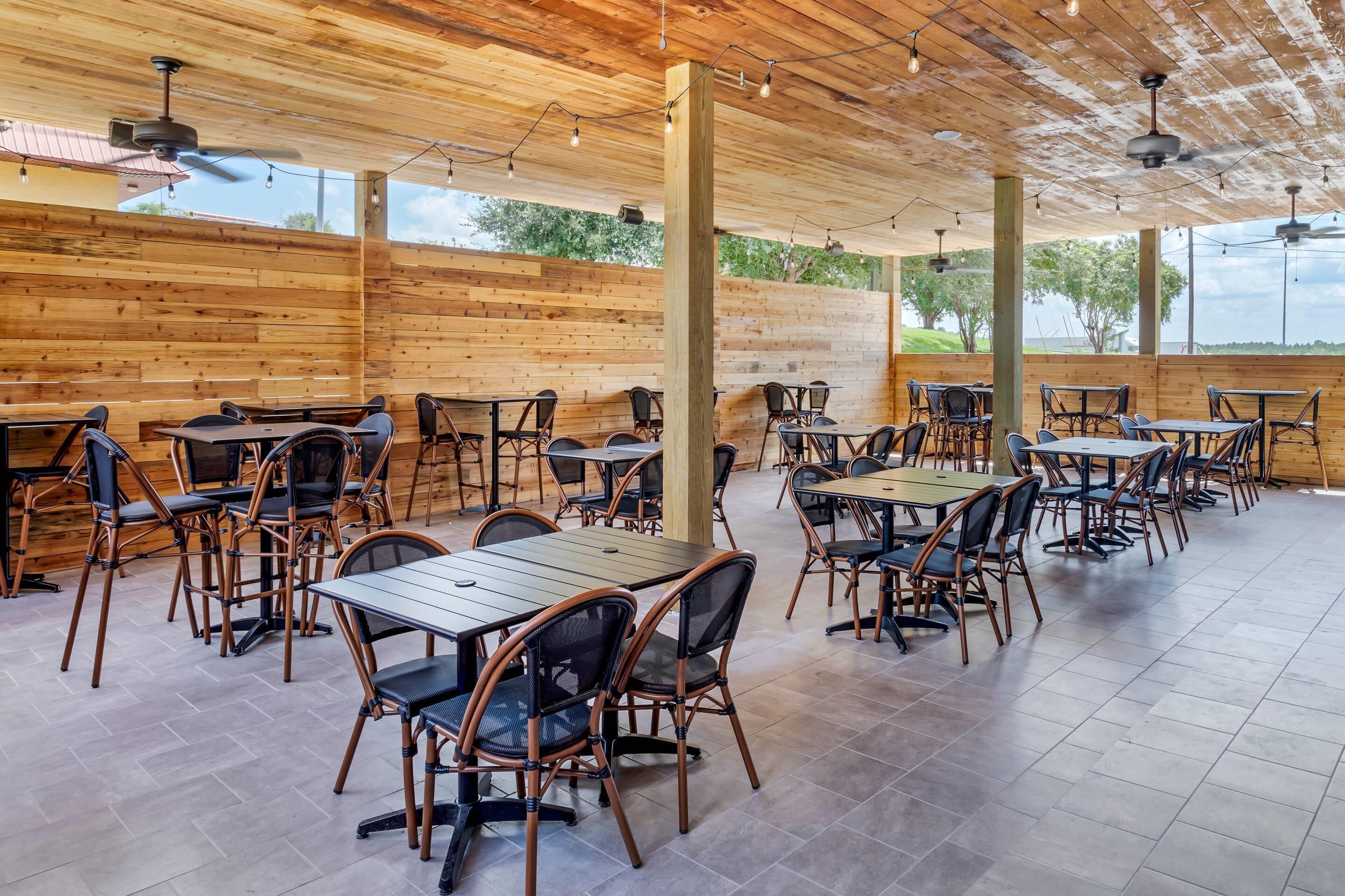 An outdoor dining area with wooden walls and ceiling, featuring multiple tables and chairs.