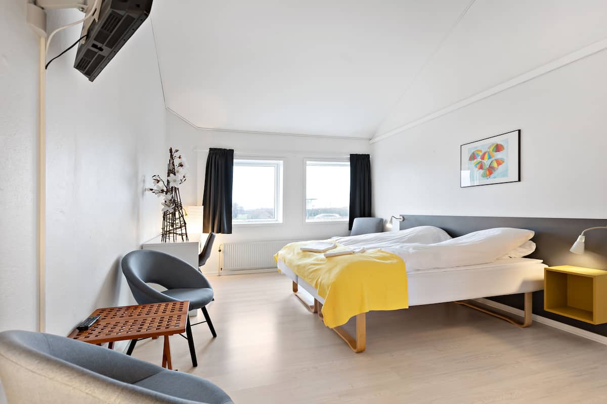 A modern hotel room with a bed, bedside table, chair, and a view of the city.