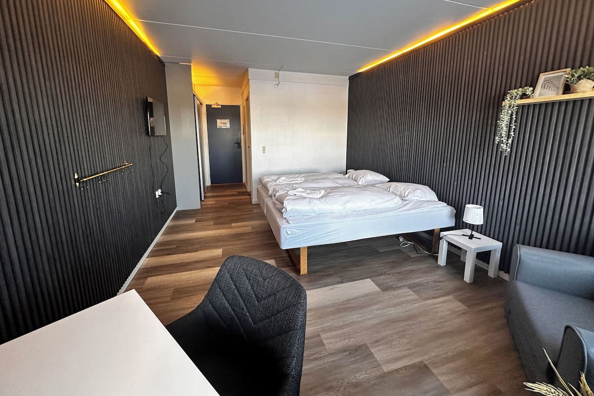 A modern hotel room with a bed, a desk, a chair, and a sofa.