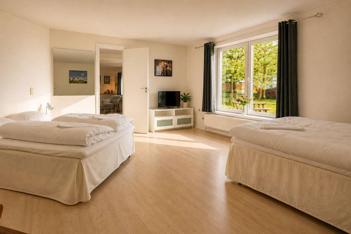 A hotel room with two beds, a TV, a small table, and a window with curtains.
