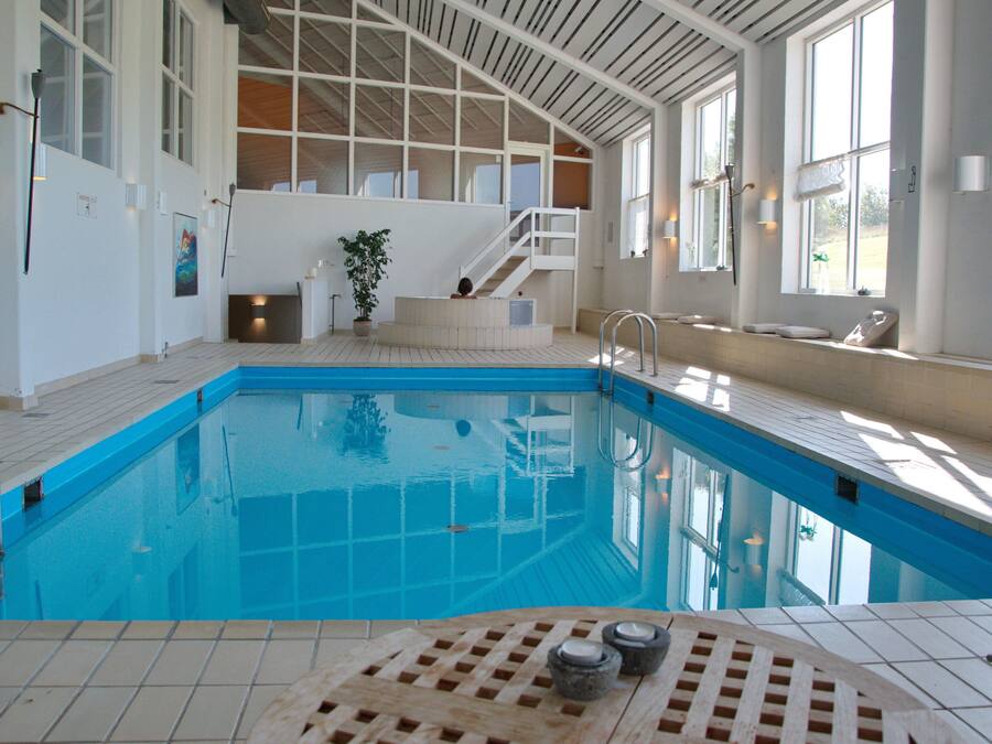 Una piscina interior con suelo de baldosas, terraza de madera y una escalera que sube a un nivel superior.