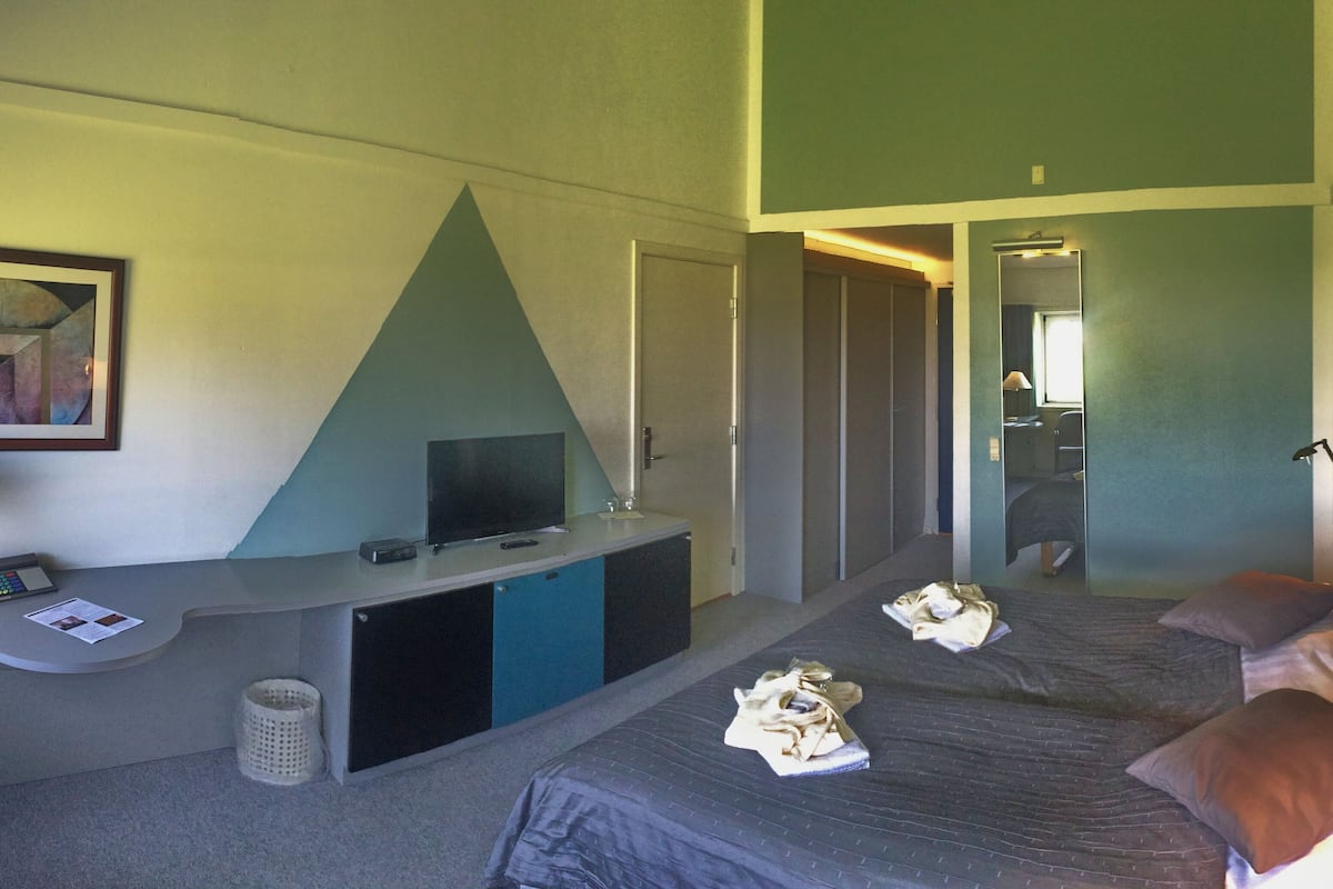 A hotel room with a bed, a desk with a computer, a TV, and a mirror.