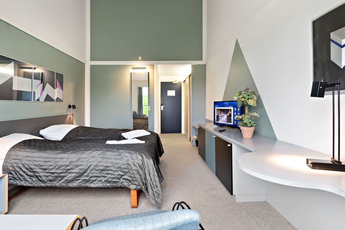 A modern hotel room with a bed, a desk, a chair, a mirror, and a television.