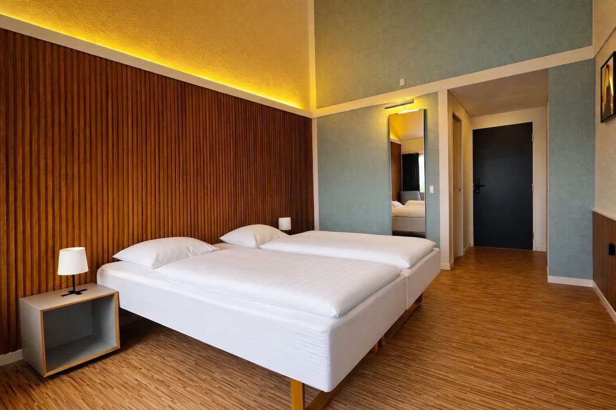 A hotel room with a large bed, a nightstand, a lamp, and a mirror.