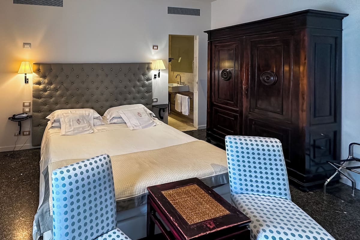 A hotel room with a large bed, two bedside tables with lamps, a wardrobe, and a chair with a polka dot cushion.