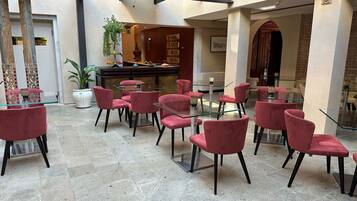 A hotel lobby with red velvet chairs and glass tables, a potted plant, and a bar area.