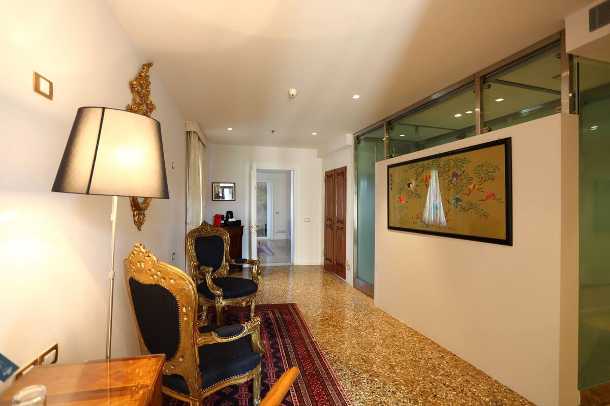 A hallway with a wooden table, ornate chairs, a patterned rug, and a framed painting on the wall.